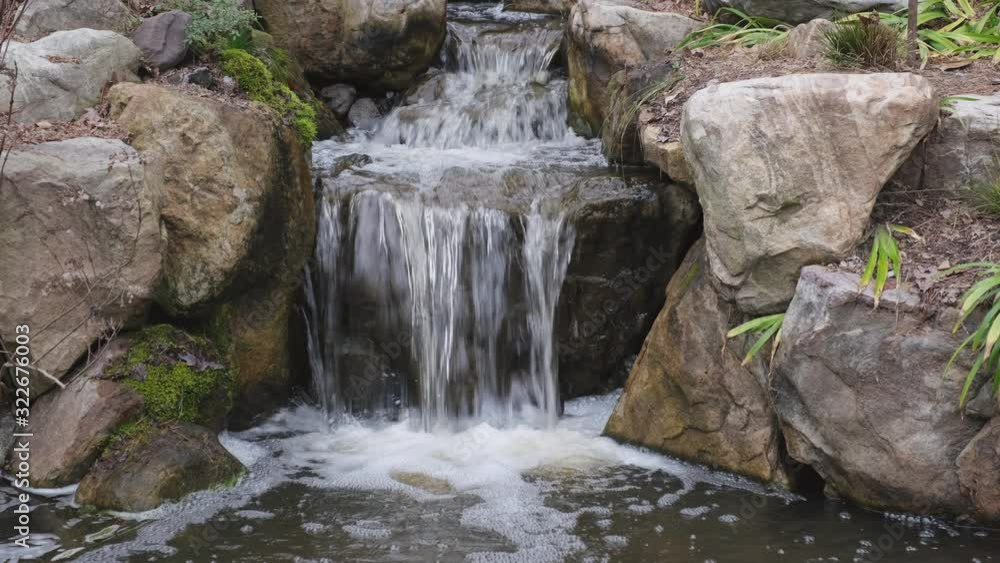 Water cascades gently down a stream and over dark brown stones in a water garden feature in Durham, North Carolina Water cascades gently down a stream and over dark brown stones in a water garden feature in Durham, North Carolina