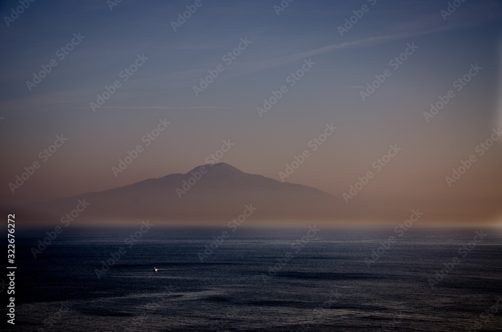 Amanecer en el mar mediterráneo con el volcán Vesubio de fondo y un pequeño barco navegando