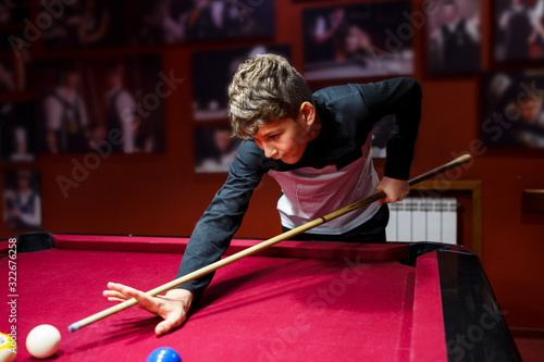 Boy plays billiard or pool in club. Young Kid learns to play snooker. Boy with billiard cue strikes the ball on table. Active Leisure, sport, hobby concept	 photo