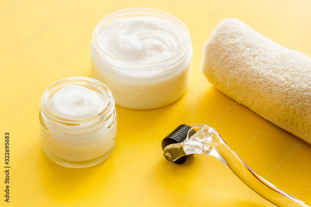 Dermaroller for home cosmetologic procedure near creams on yellow background Dermaroller for home cosmetologic procedure near creams on yellow background