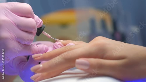 Manicurist master is covering painting client's nails shellac, hands closeup. Professional manicure in beauty salon. Hygiene and care for hands. Beauty industry concept. photo
