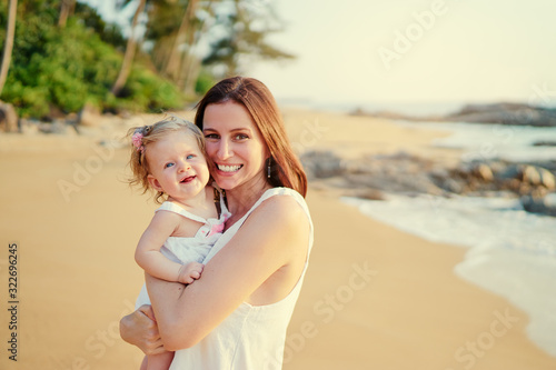 Portrait of happy young mother holding little daughter on the tropical beach. © luengo_ua