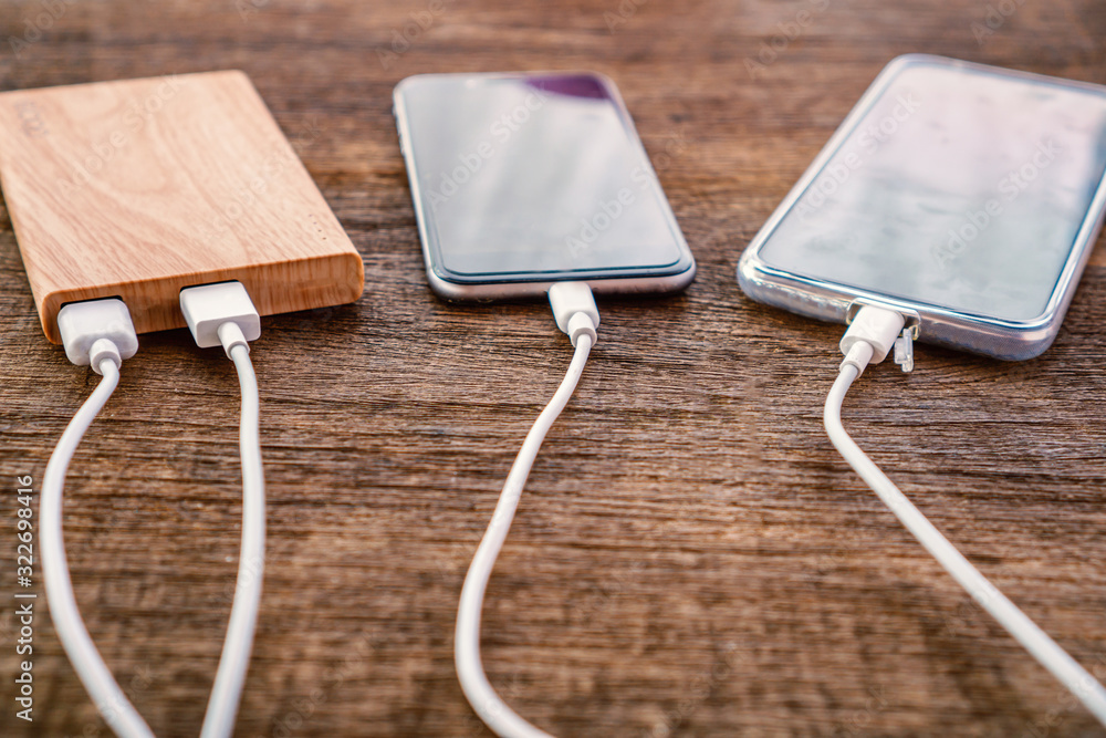 two smart phone charging with power bank on wooden table two smart phone charging with power bank on wooden table