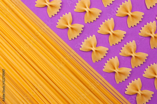 Raw pasta farfalle and spaghetti on purple background with copyspace.
