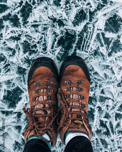 Russia. Lake Baikal. Cracked ice of Baikal. March. One can see legs in black jeans and trekking boots that stand on cracked ice. Ice pattern
