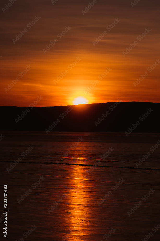 Baikal. Island Olkhon. Orange sunset with clouds. Reflection on ice