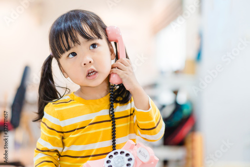 3 years old little asian girl holding vintage telephone talking and listening to her dad or father. Asian child girl call delivery food service in the morning.Children and vintage technology concept. photo