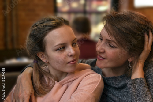 mother and adult daughter teenager are sitting at a table in a cafe, looking at each other