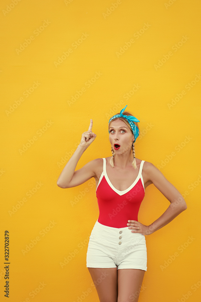 Your text here. Amazed beautiful young woman pointing up while standing against yellow wall. Your text here. Amazed beautiful young woman pointing up while standing against yellow wall.
