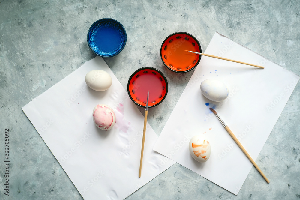 top view selective focus cups with dye, brushes and white eggs on a concrete background, painting eggs for Easter diy concept top view selective focus cups with dye, brushes and white eggs on a concrete background, painting eggs for Easter diy concept