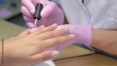 Manicurist master is covering painting client's nails shellac, hands closeup. Professional manicure in beauty salon. Hygiene and care for hands. Beauty industry concept.