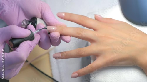 Manicurist master is covering painting client's nails top coat shellac, hands closeup. Professional manicure in beauty salon with gel polish. Hygiene and care for hands. Beauty industry concept. photo