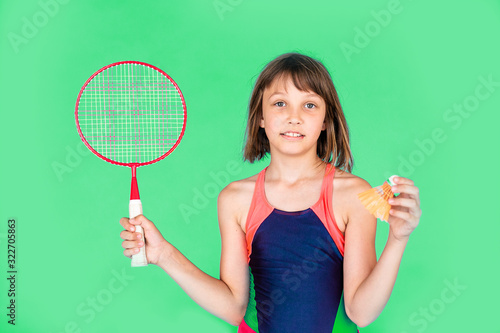 Young teenager girl jumping and playing badminton on green background