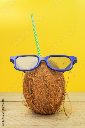 A coconut with green paper straw wearing 3D glasses on yellow background. Summer and trave concept
