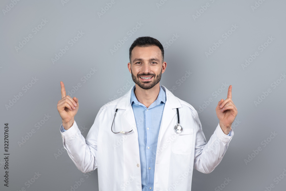 Bearded doctor in a white robe pointing upwards Bearded doctor in a white robe pointing upwards