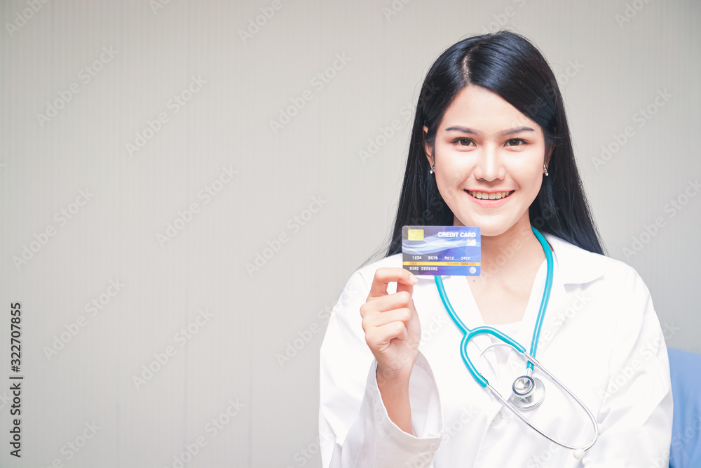 Beautiful Asian doctor holding a credit card standing smiling brightly White backdrop. Health service concept And finance in one card Beautiful Asian doctor holding a credit card standing smiling brightly White backdrop. Health service concept And finance in one card
