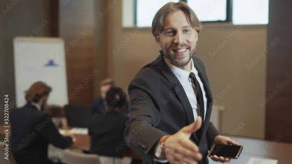 Business meeting, businessman uses a mobile phone, man in a suit typing on smartphone, holds out his hand, colleagues communicate in the blurred background. Business meeting, businessman uses a mobile phone, man in a suit typing on smartphone, holds out his hand, colleagues communicate in the blurred background.