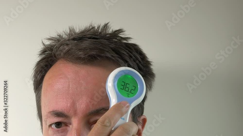 Man Takes Temperature With Digital Thermometer On Forehead