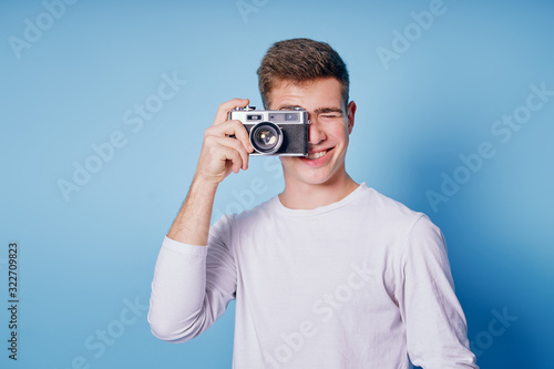 Traveler and photographer. Studio portrait of handsome young man holding photocamera taking photo. Blue blackground.