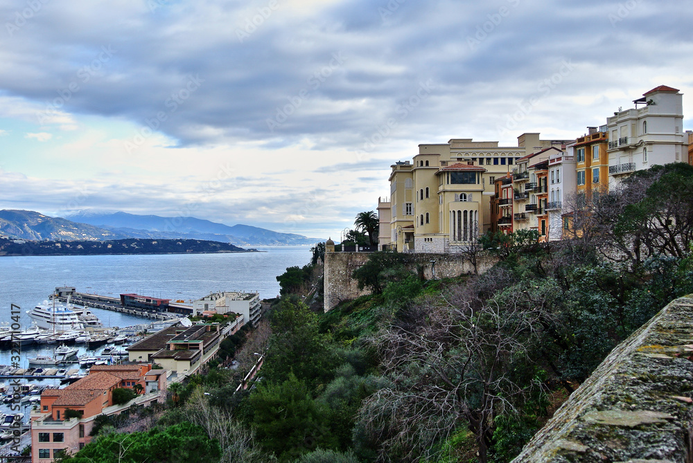 Monte Carlo, Monaco - Houses in bright colors on the shores of the Mediterranean Sea, a bay with moorings on which there are yachts, the sky with white-gray clouds.