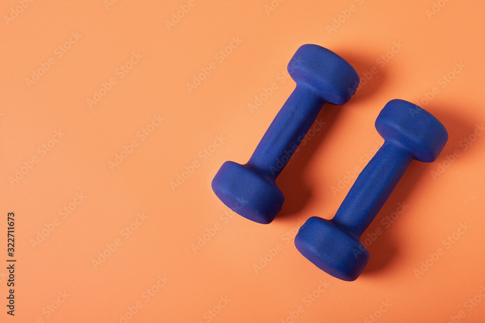 Blue dumbbells Isolated on orange background. Top view. Copy space. Blue dumbbells Isolated on orange background. Top view. Copy space.