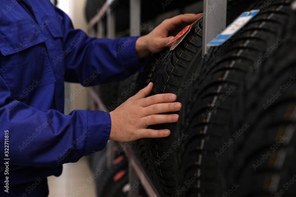 Male mechanic with car tire in auto store, closeup