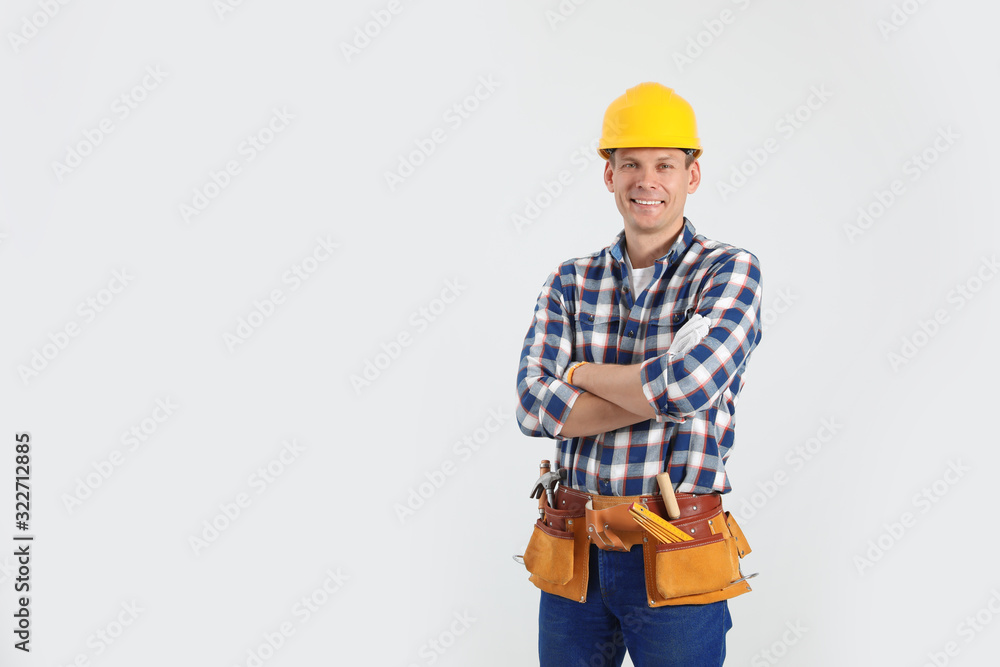 Handsome carpenter with tool belt on light background. Space for text Handsome carpenter with tool belt on light background. Space for text