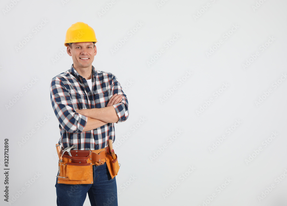 Handsome carpenter with tool belt on light background. Space for text Handsome carpenter with tool belt on light background. Space for text