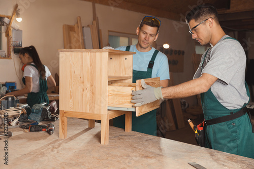 Professional carpenters assembling wooden cabinet in workshop