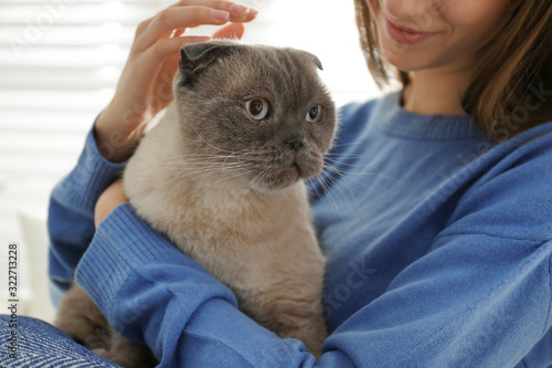 Young woman with cute cat at home, closeup. Fluffy pet