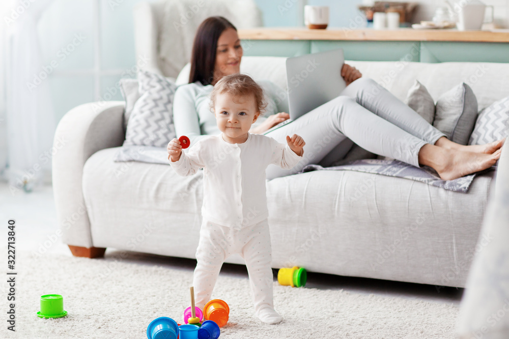 Mom works at a laptop at home while her child is playing. Business and family concept.