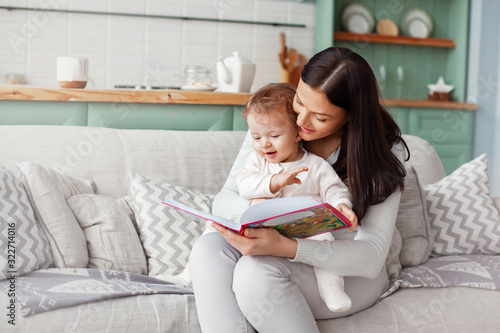 Mom sits on a sofa with a child, reads a book and looks at bright pictures