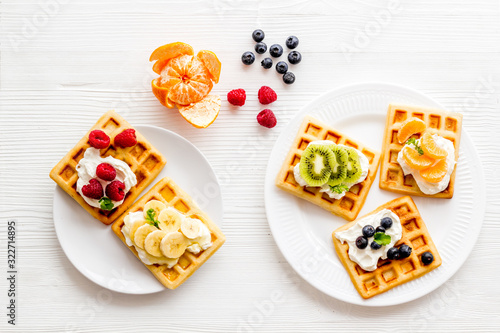 Belgian waffles with creamy cheese and berries on white background top-down