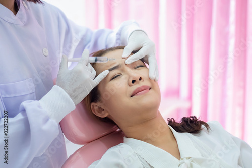 Beautiful women are injecting Botox in the face. The medical specialist is holding a syringe and injecting it on her forehead.