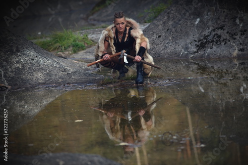 A strong woman, a feminist, a symbol of feminism. Viking woman with axe in a traditional warrior clothes. Against the backdrop of a large viking village photo