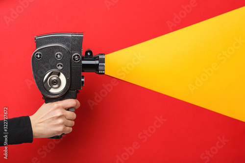 Female hand holding old style film movie camera imitating shooting process on a red background photo