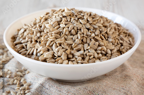 Raw Sunflower Seed Kernels in a white bowl on a white wooden background, side view. Close-up.