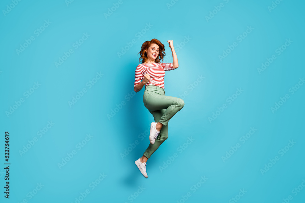 Goal. Full size profile photo of funny pretty lady jump high up raise fists winner sports competition wear casual red white shirt green trousers shoes isolated blue color background