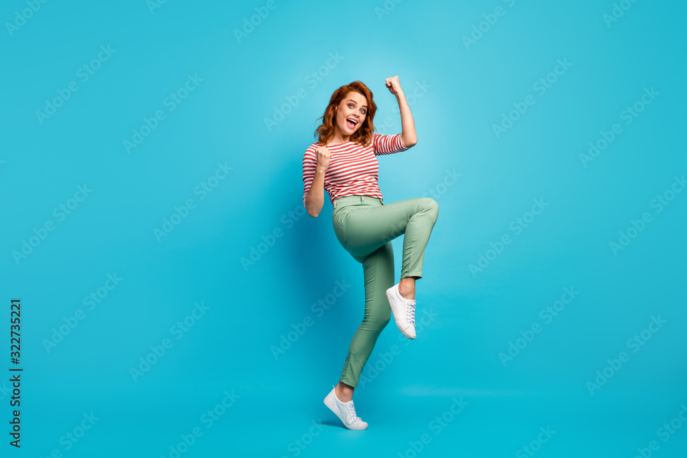Yeah. Full length profile photo of beautiful lady crazy emotions raise fists win money lottery wear casual red white shirt green pants footwear isolated blue color background