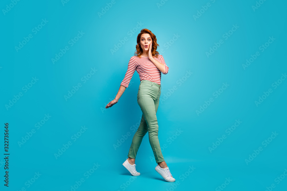 Full length profile photo of pretty lady enjoy warm spring day walk street see sale advert banner wear casual red white shirt green pants footwear isolated blue color background Full length profile photo of pretty lady enjoy warm spring day walk street see sale advert banner wear casual red white shirt green pants footwear isolated blue color background