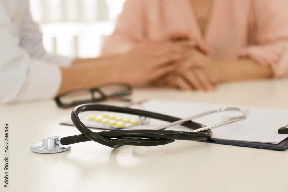 Closeup view of doctor holding senior patient's hands in office, focus on stethoscope Closeup view of doctor holding senior patient's hands in office, focus on stethoscope