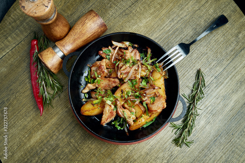 Fried potatoes with bacon, onions and herbs in a decorative pan on a wooden background. Top view on tasty food.