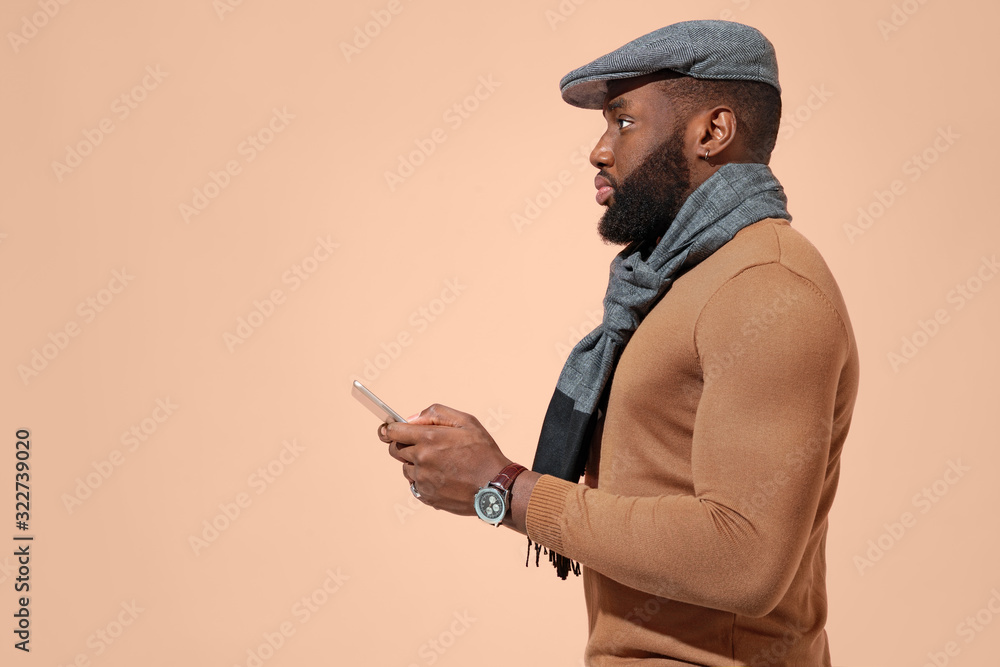 Handsome man uses the tablet, checks for news. Photo of african man in stylish casual clothes on beige background. Handsome man uses the tablet, checks for news. Photo of african man in stylish casual clothes on beige background.