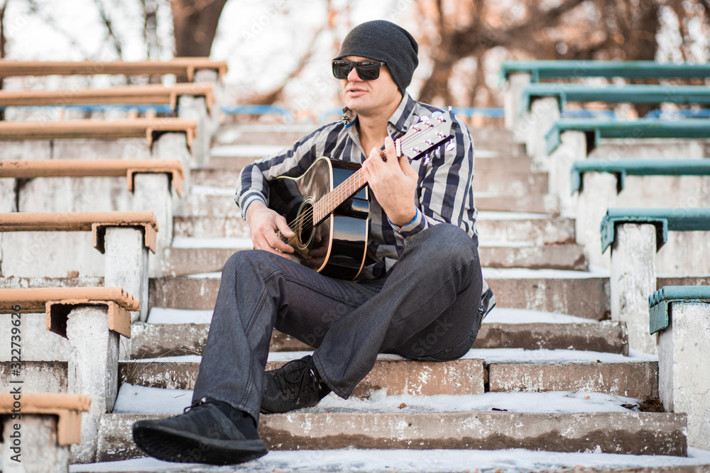 Young man sitting on steps playing guitar and singing, music concept Young man sitting on steps playing guitar and singing, music concept