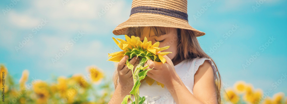 A child in a field of sunflowers. Selective focus. - obrazy, fototapety, plakaty 