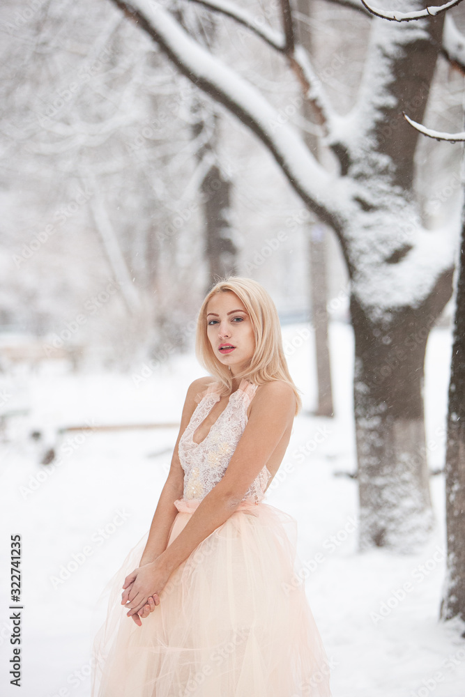 A beautiful young blond woman in a white dress posing in a snowy winter park