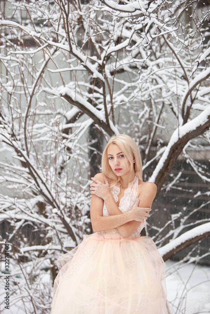 A beautiful young blond woman in a white dress posing in a snowy winter park A beautiful young blond woman in a white dress posing in a snowy winter park