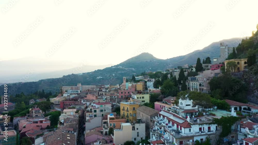 Drone rotates rising over the old city of Taormina in southern Italy; colorful buildings against mountains covered by a sunlight during a golden hour. Drone rotates rising over the old city of Taormina in southern Italy; colorful buildings against mountains covered by a sunlight during a golden hour.
