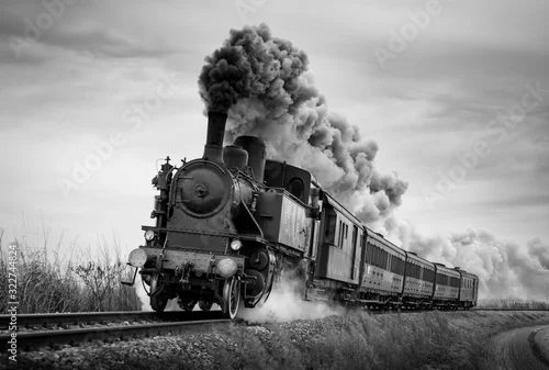 Obraz Steam train runs on the tracks on a cloudy day. Black and white photography.