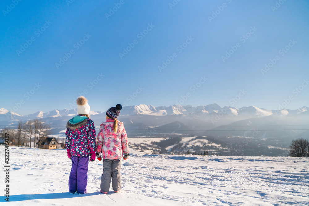 Back view of children standing on rural roadway in snow looking at mountain range in sunshine